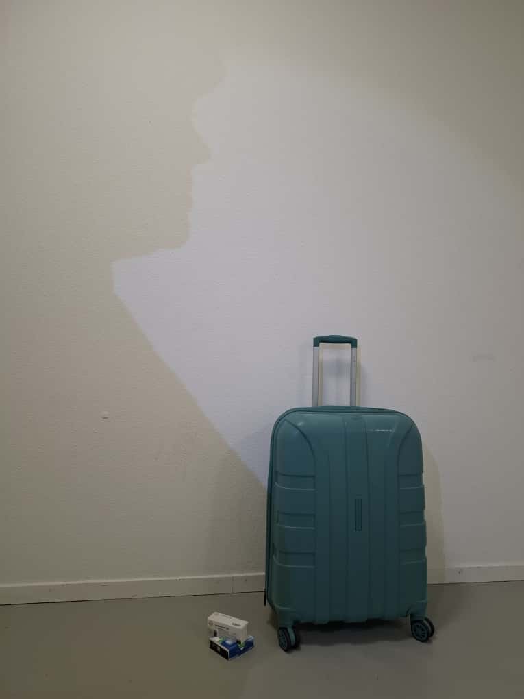 [English] A suitcase… It stands before me like a sealed past. No matter how far I go, its contents always follow. Beneath it, a few boxes of pills. Small, silent witnesses. Each one a proof of the day my body whispered, “endure.” Every pill swallowed feels like a little less hope remaining. And on top of the suitcase, a shadow falls… My shadow. But sometimes even I don’t recognize it. Because this shadow isn’t only mine. It’s the system’s weight pressing down on me. For being “too much,” for being “different,” for daring to be “seen.” To be queer, to be a refugee— it’s to breathe and drown at the same time. You want to live, yet each day you live feels a little more like dying. Health, you say? Here, health is not a right… It’s an exam. You must leave a thousand identities behind just to pass through one door. Say “I’m trans,” and their eyes change. Say “I’m a refugee,” and the doors close. Sometimes I sit beside that suitcase, staring at the pills… Each one whispers to me: “Hold on, your place is still not here.” But even my shadow exhausts me now. Because sometimes, even your own shadow abandons you. Still… A quiet sentence runs through me: “They broke me, but I’m still here.” And that sentence becomes the heaviest suitcase my heart will ever carry.